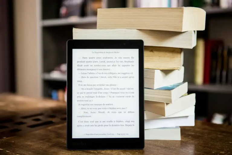 e-reader-with-text-displayed-next-to-a-stack-of-physical-books-on-a-wooden-table