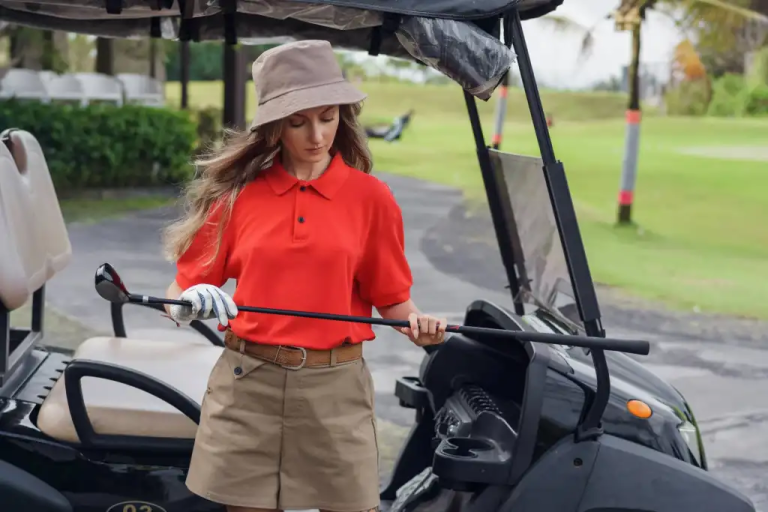 woman-in-red-and-khaki-golfing-outfit-standing-by-a-cart-holding-a-golf-club-on-a-sunny-day